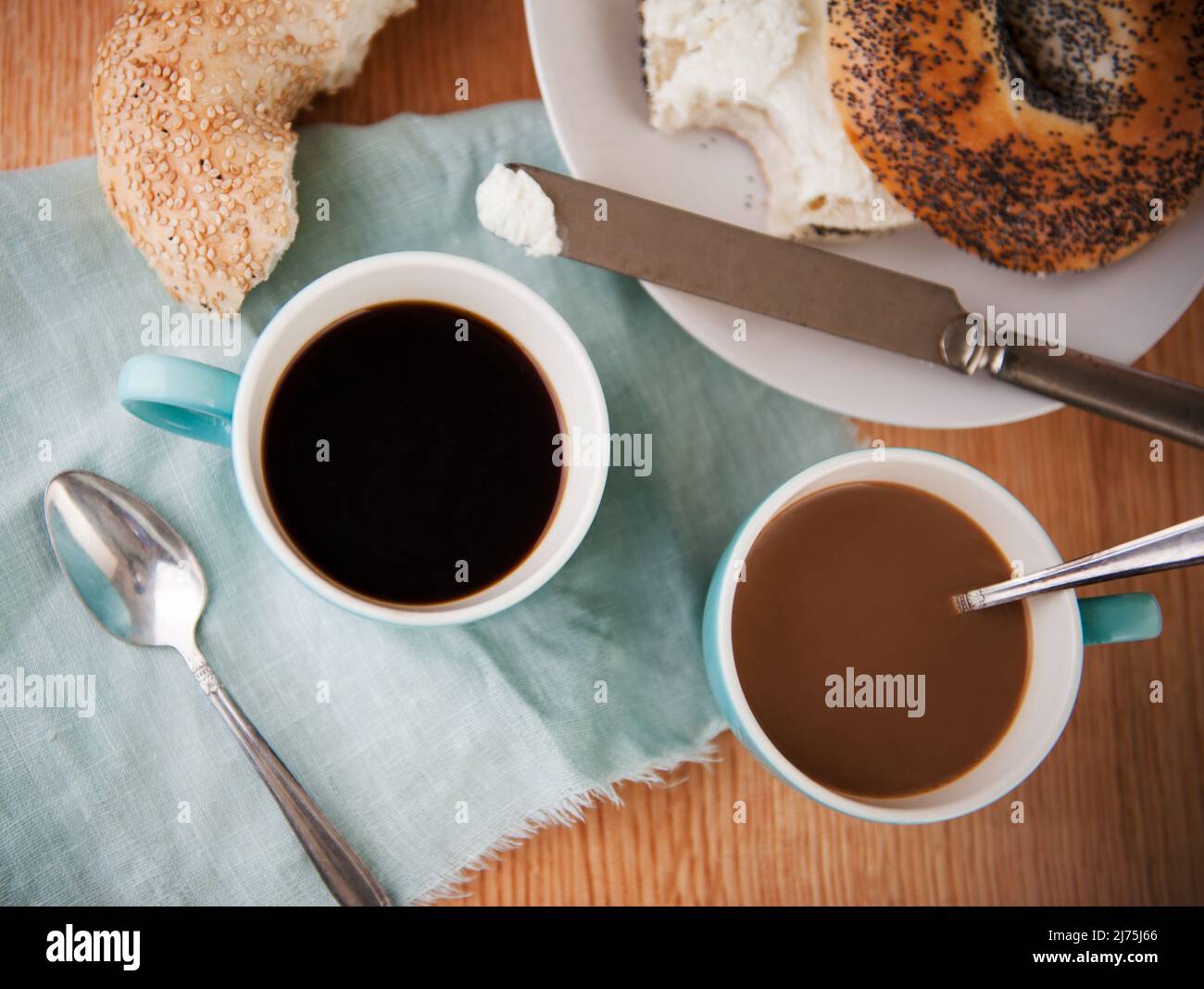 Zwei Tassen Kaffee mit braunen Zuckerwürfeln; Poppy Seed Bagel im Hintergrund Stockfoto
