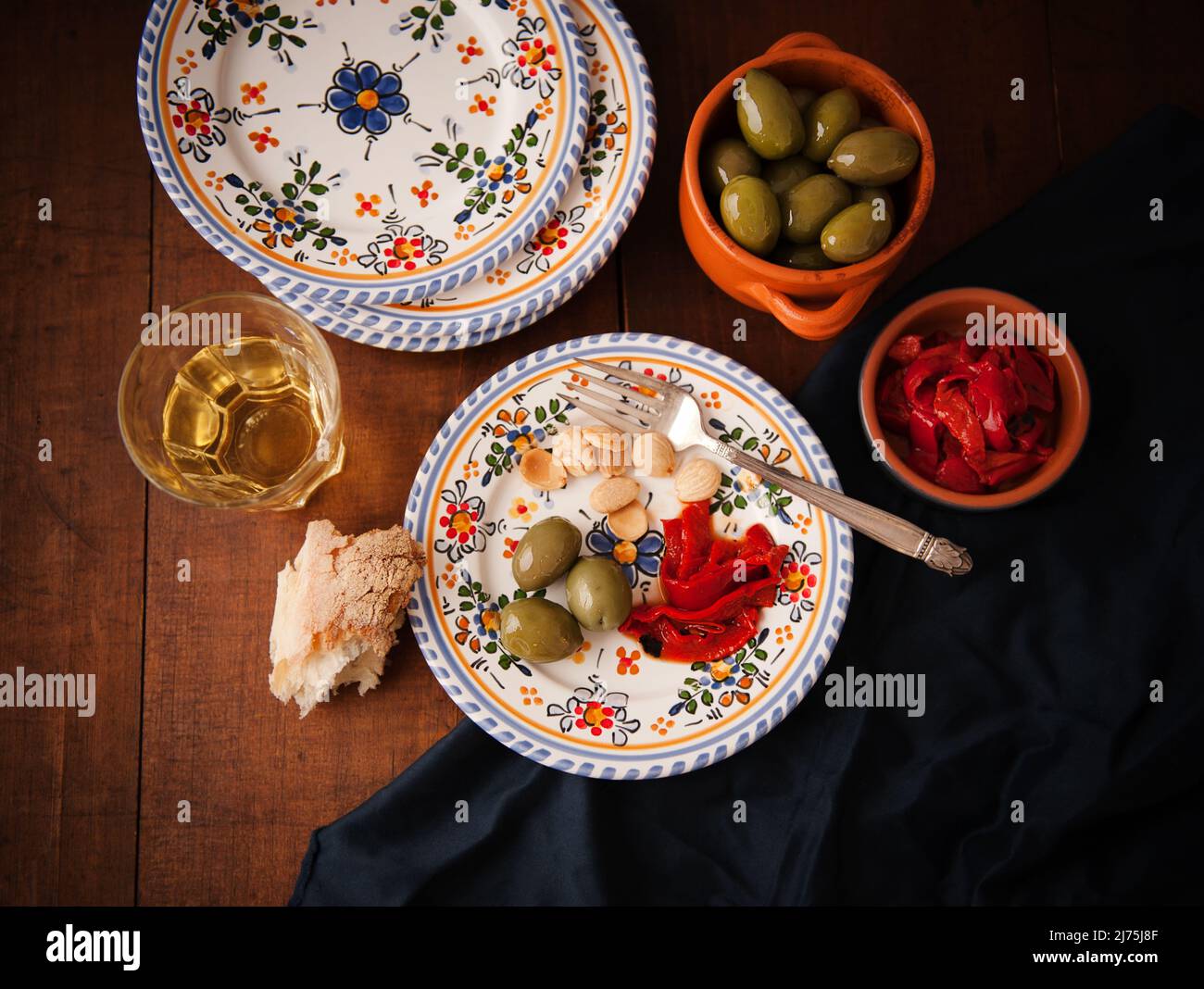 Teller mit einer einzigen Portion Tapas, grünen Oliven, gerösteten roten Paprika und Mandeln, Brot und Weißwein Stockfoto