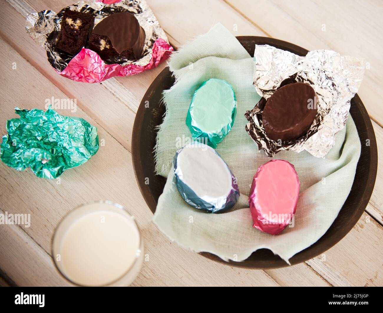 Mini Cream gefüllte Schokoladenkuchen in farbigen Folienverpackungen mit einem Glas Milch Stockfoto