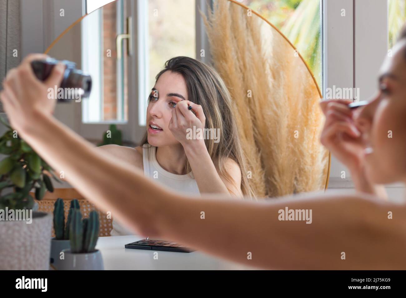 Junge schöne Frau tut ihr Make-up und Lidschatten, während sie kosmetische Bewertung und hält Vlogging-Kamera Stockfoto