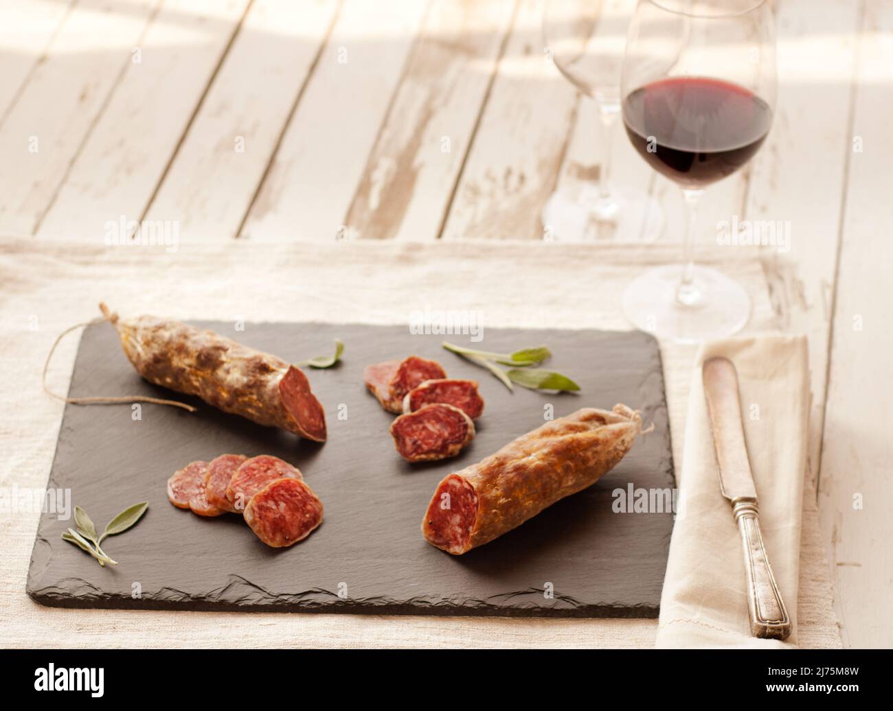 Salami; teilweise auf Schiefertau geschnitten; Glas Rotwein Stockfoto