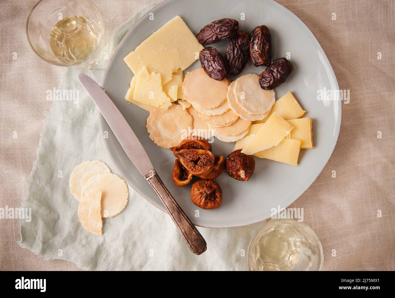 Cheddar-Käse mit Crackern, Feigen und Pflaumen auf einem Teller; mit Weißwein; von oben Stockfoto