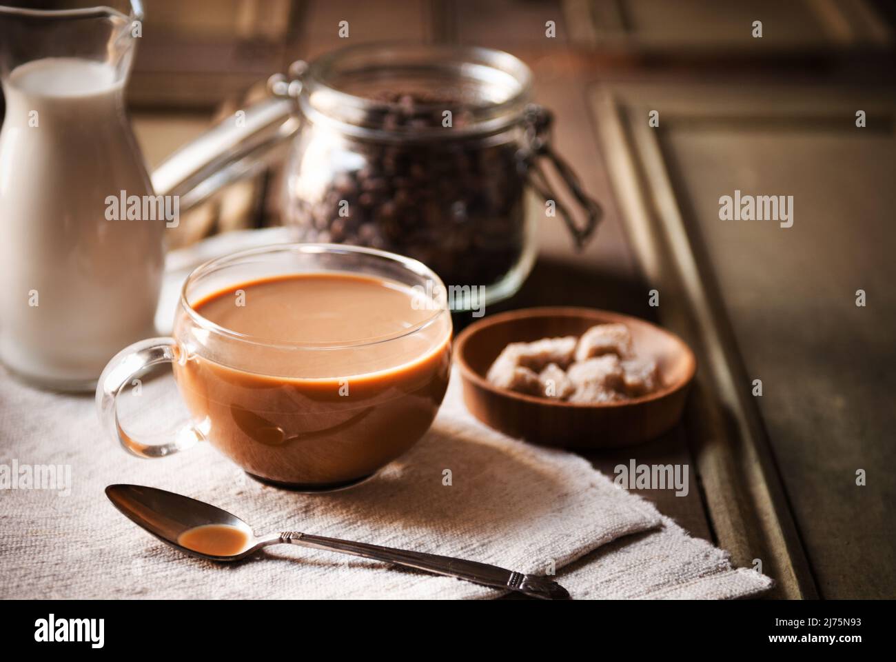 Milchkaffee in einer Glasschale; Kaffeebohnen im Hintergrund Stockfoto