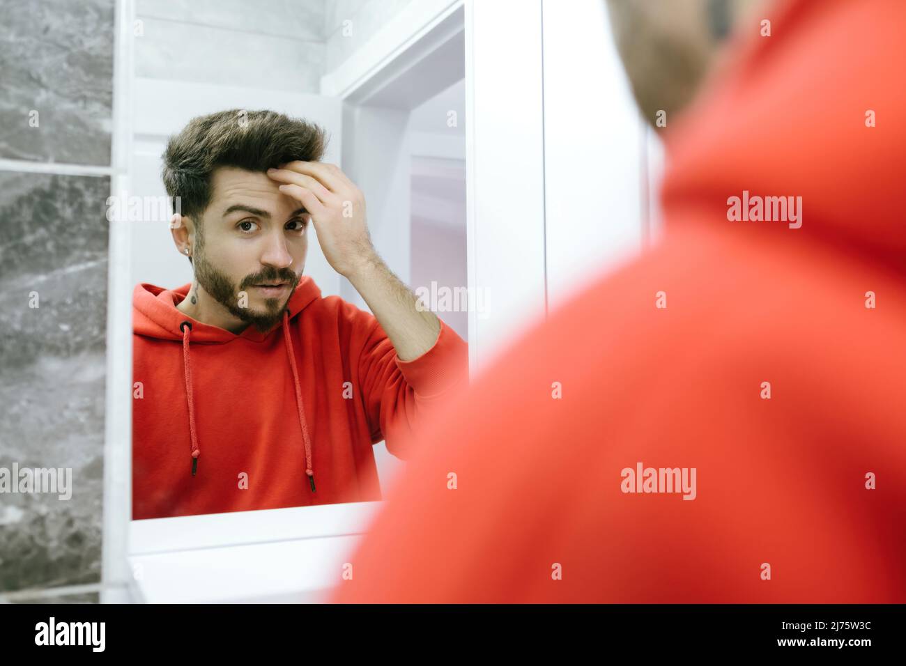 Vor dem Spiegel posiert der junge Mann, der seine Hände an sein Haar nimmt, während sich ein erwachsener Mann darauf vorbereitet, ins Badezimmer zu gehen Stockfoto