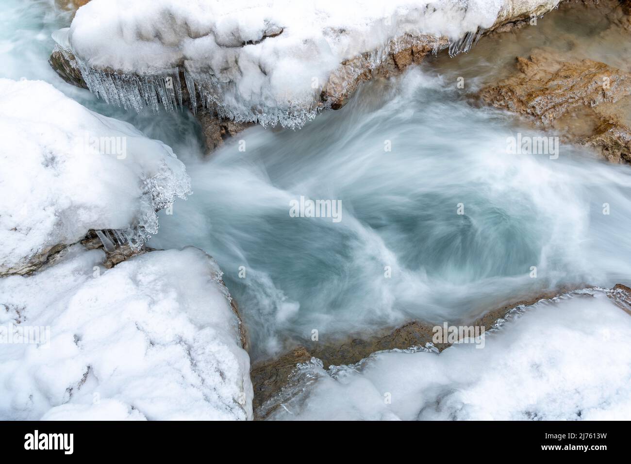 Eiszapfen hängen über dem klaren Wasser des Rissbaches in Tirol an einem schmalen Punkt bei Hinterriss. Stockfoto