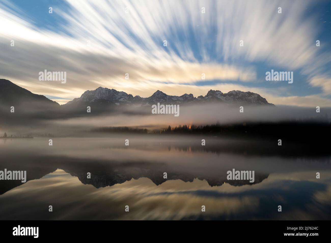 Nächtliche, lange Exposition der Wolken und Nebel im Herbst, mit dem Karwendelgebirge im klaren Wasser des Barmsee bei Krün reflektiert. Stockfoto