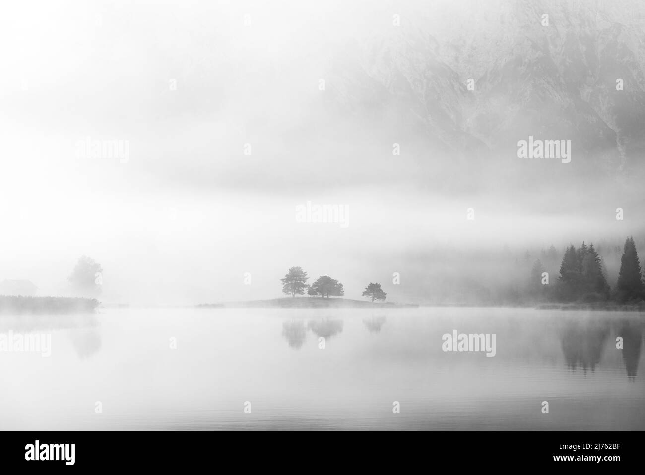Herbststimmung an einem kleinen See in den bayerischen Alpen, im Hintergrund das Karwendelgebirge, eine kleine Halbinsel im Nebel und die Spiegelung im Wasser. Fast mystisch ist die Nebelatmosphäre mit den schroffen Bergen. Stockfoto