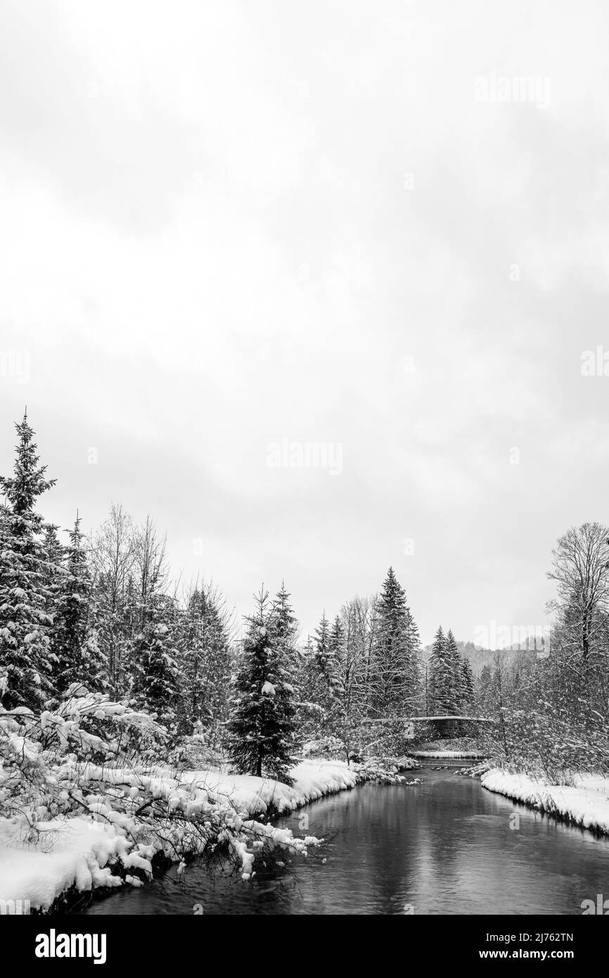 Alte Steinbrücke auf der Obernach zwischen Wallgau und Walchensee im Winter mit dichtem Schnee und Wolken. Der kleine Bach schlängelt sich durch die Winterlandschaft Stockfoto