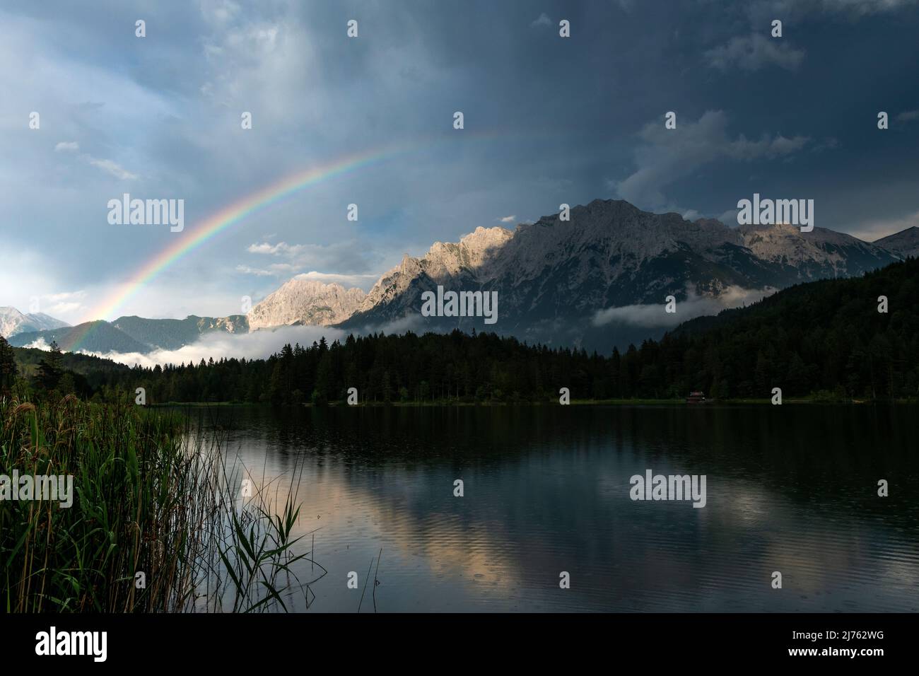 Der Lautersee, ein kleiner See in den bayerischen Alpen, oberhalb von Mittenwald. Im Hintergrund das Karwendel, bei Regen und Gewittern zieht sich ein Regenbogen über das Wasser. Stockfoto