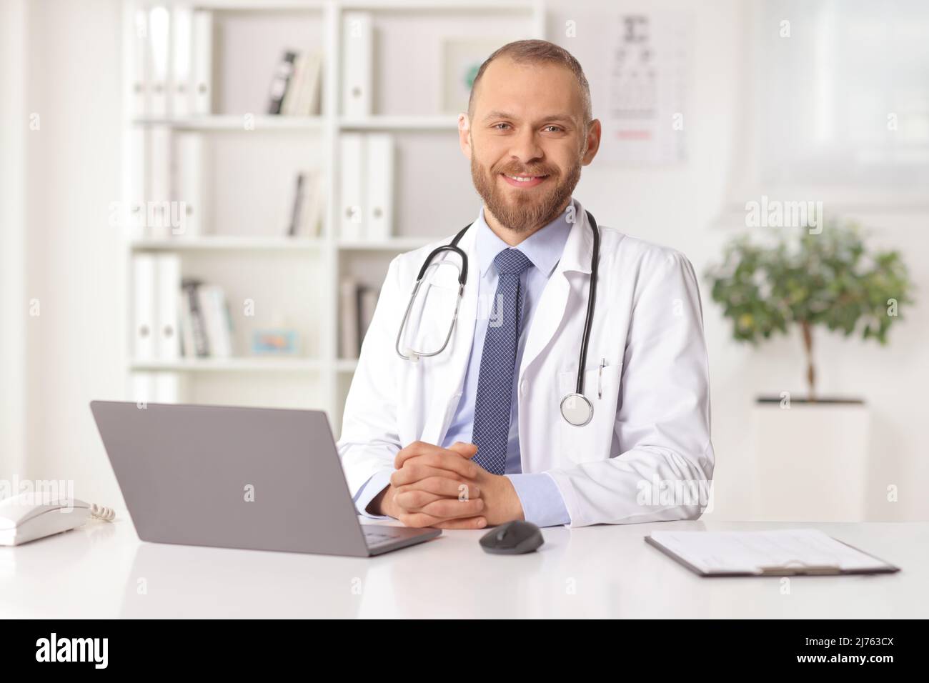 Junger Arzt, der in einem Büro mit einem Laptop auf dem Schreibtisch sitzt Stockfoto