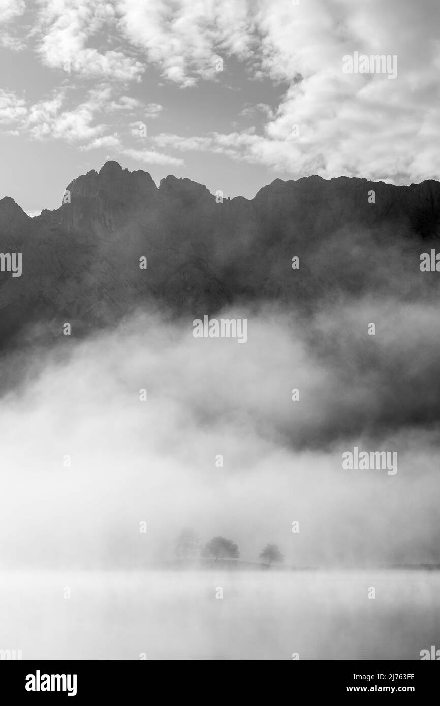 Herbststimmung an einem kleinen See in den bayerischen Alpen, im Hintergrund das Karwendelgebirge, eine kleine Halbinsel im Nebel und die Spiegelung im Wasser. Fast mystisch ist die Nebelatmosphäre mit den schroffen Bergen. Stockfoto
