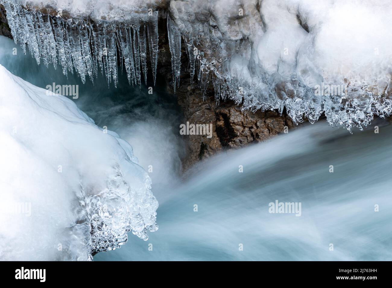 Eiszapfen hängen über dem klaren Wasser des Rissbaches in Tirol an einem schmalen Punkt bei Hinterriss. Stockfoto
