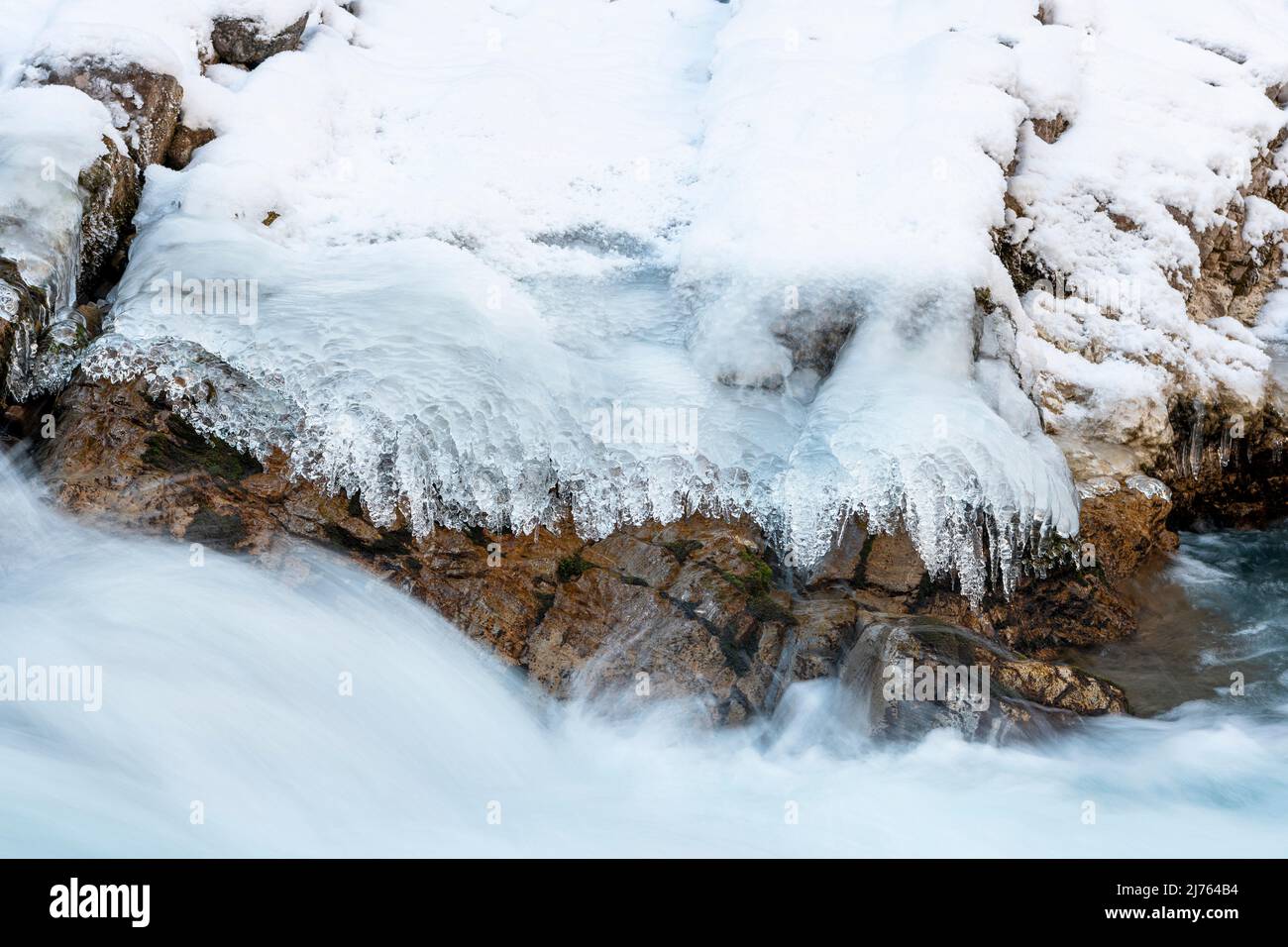Schnelles Wasser des Rissbaches bildet Spray und Strom. Eisstrukturen und Felsen, die am Ufer des Gebirgsbaches gebildet werden, Grenzen das Bild ein. Aufgenommen im Winter in Tirol, Österreich im eng, nahe dem Ahornboden. Stockfoto