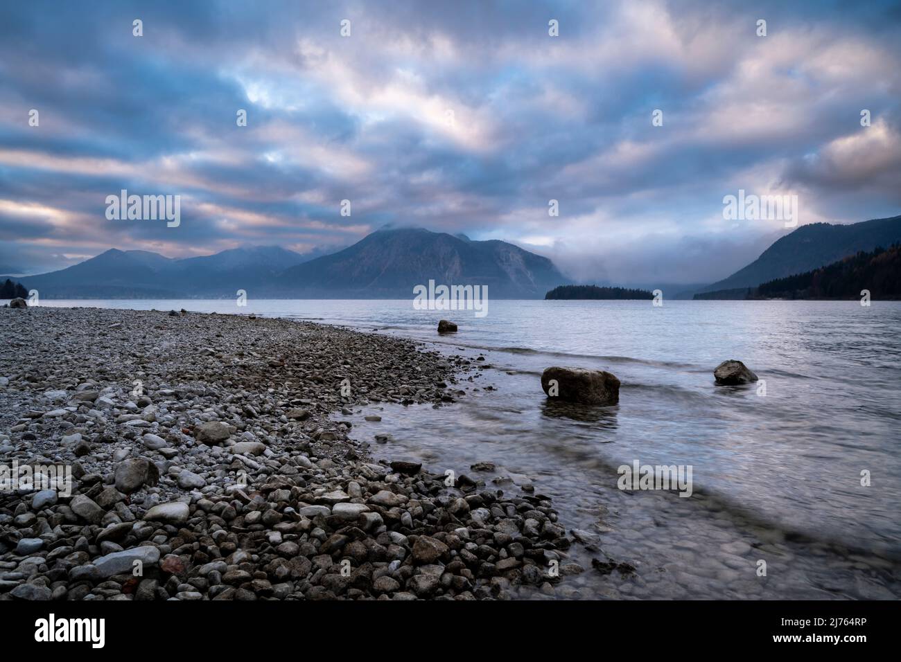 Abendstimmung mit bunten Wolken am Walchensee mit kleinen Wellen und Steinen. Stockfoto