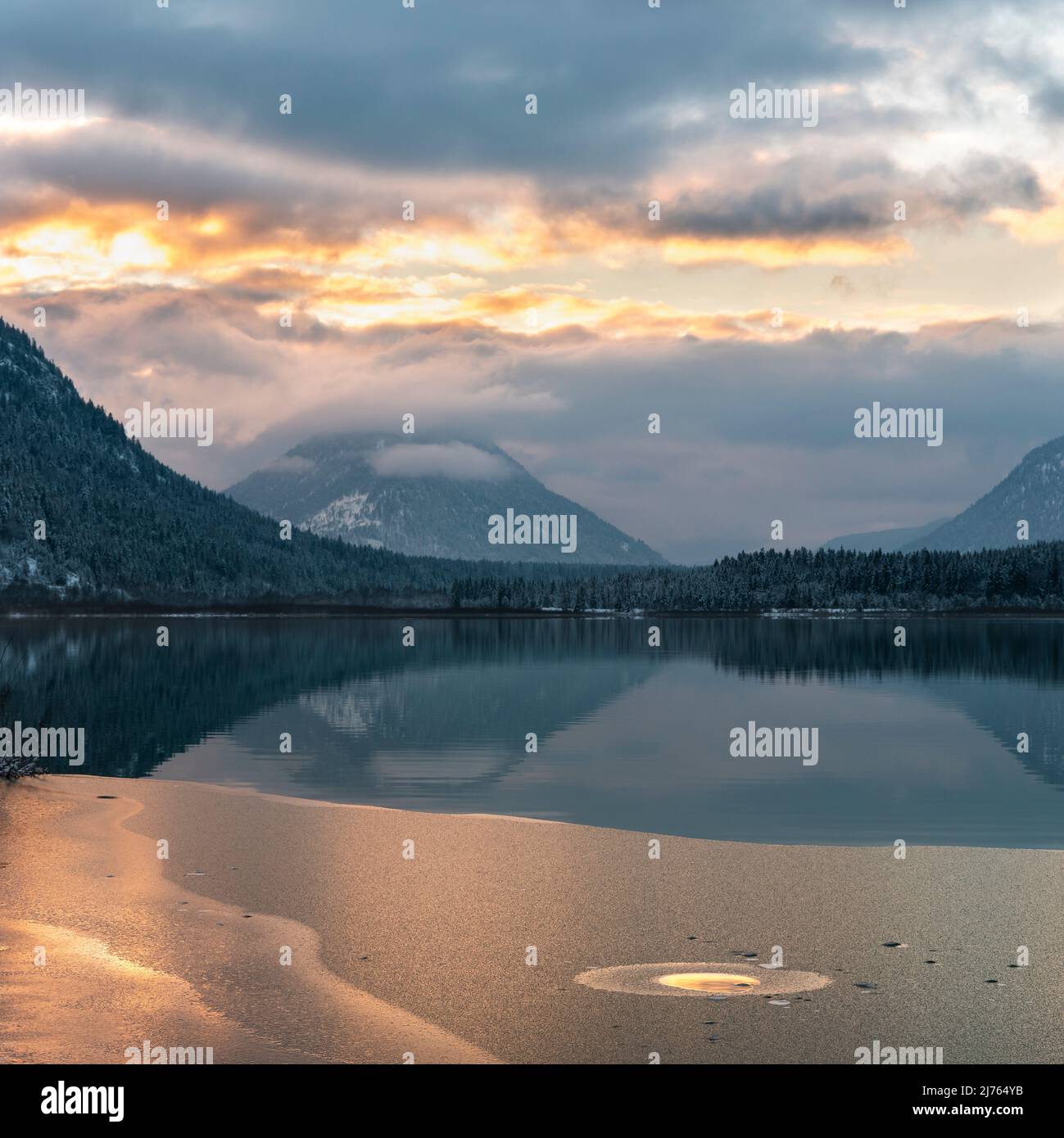 Die Farben des Sonnenuntergangs spiegeln sich im Wasser und der beginnenden Eisschicht des Sylvenstein-Stausees, im Hintergrund das Karwendelgebirge Stockfoto