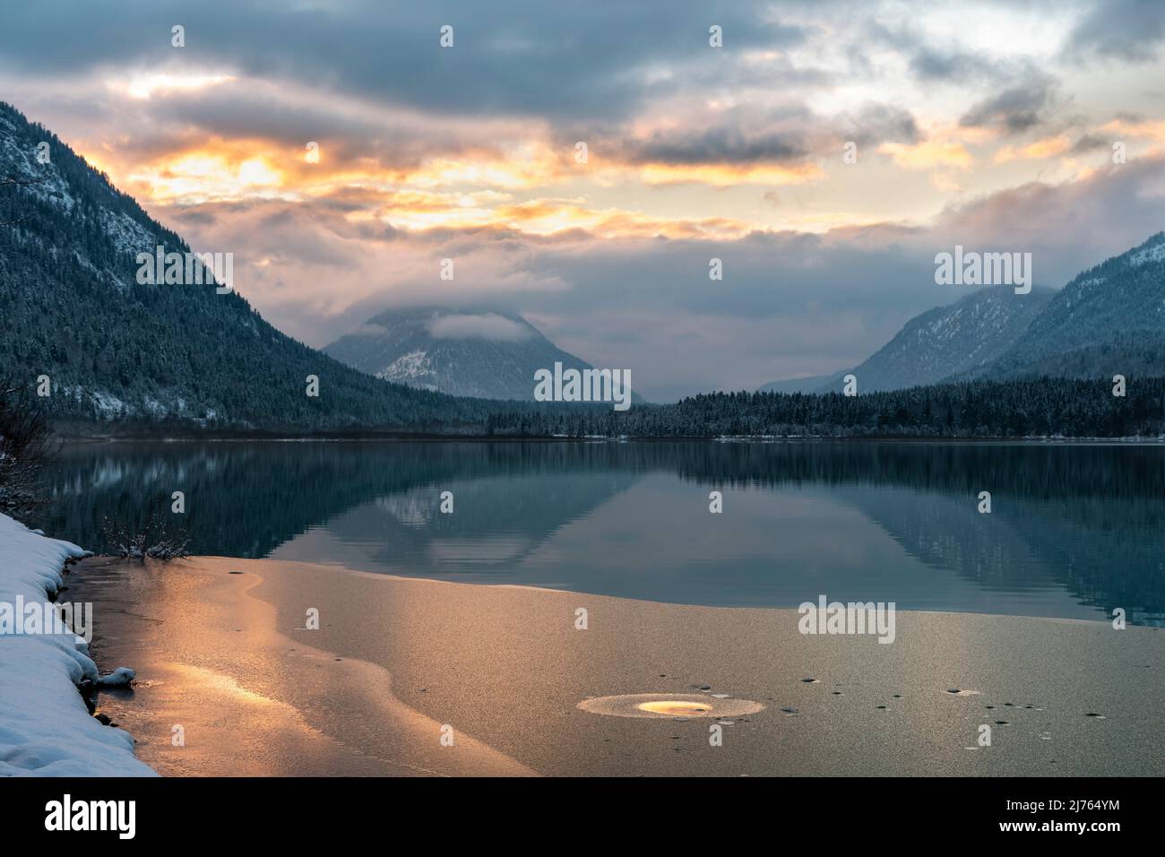 Die Farben des Sonnenuntergangs spiegeln sich im Wasser und der beginnenden Eisschicht des Sylvenstein-Stausees, im Hintergrund das Karwendelgebirge Stockfoto