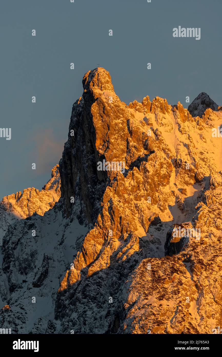Die Viererspitze (2054 m ü.d.M.) oberhalb von Mittenwald, unterhalb der westlichen Karwendelspitze, als Teil des nördlichen Karwendel-Gebirges im Abendglühen der untergehenden Sonne in roten und orangen Farbtönen gegen einen blauen Himmel im Winter mit Schnee. Stockfoto