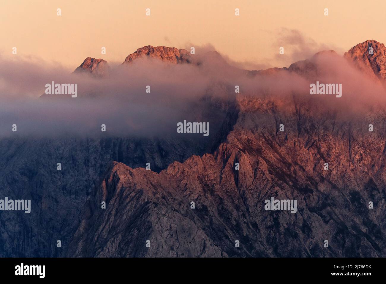 Die Schlichtenkarspitze und die Steinkarspitze leuchten rot, alpenglow kurz vor Sonnenuntergang im Karwendel, einem Teil der Alpen. Das Plankengestein wird nur durch eine leichte Wolkenschicht aufgeweicht. Stockfoto