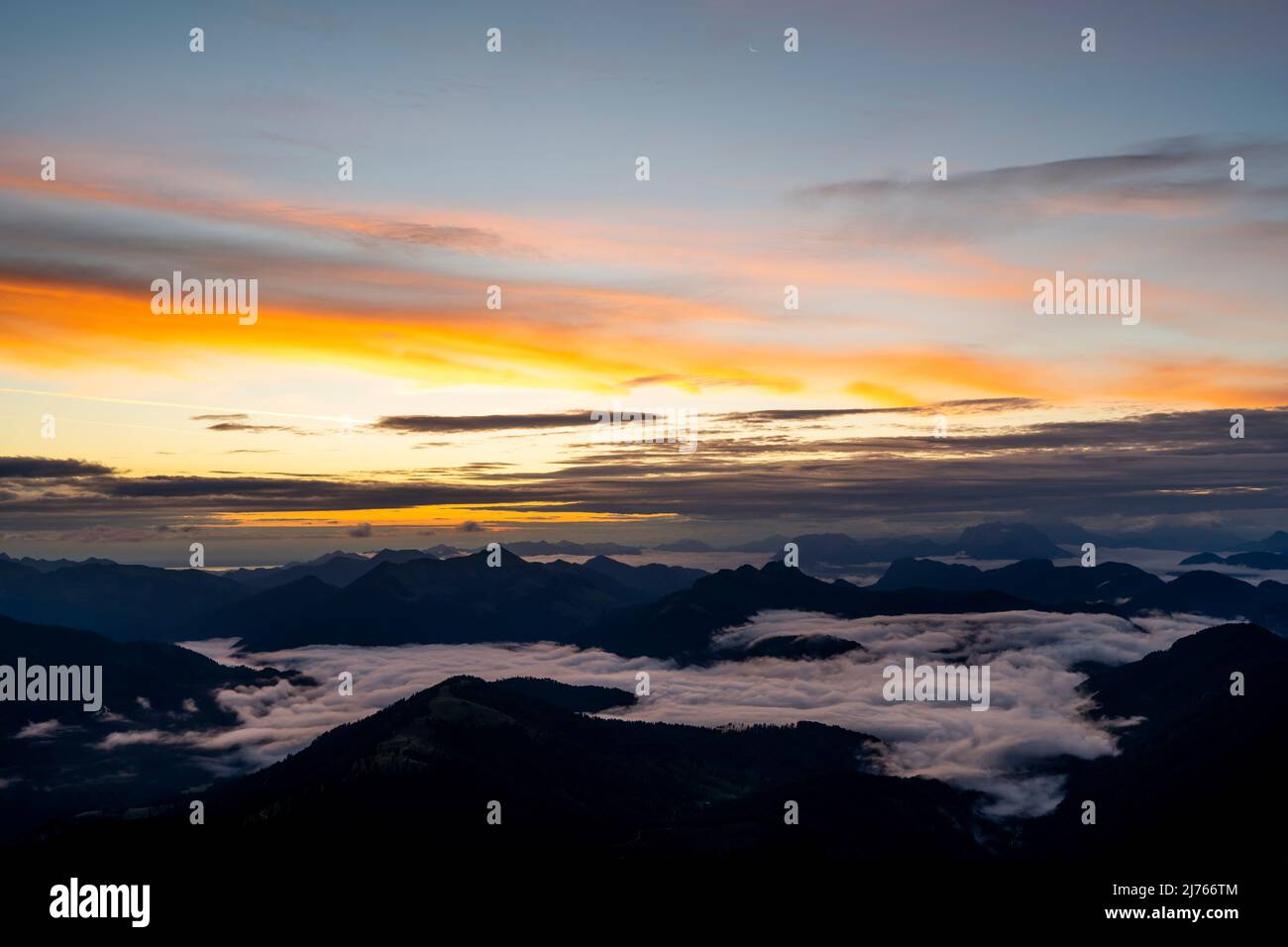 Sonnenaufgang mit Sonnenstern und hellen Wolken, während sich im Tal Nebel und Wolken bewegen. Blick von Guffert (2194m) in Rofan am frühen Morgen. Stockfoto