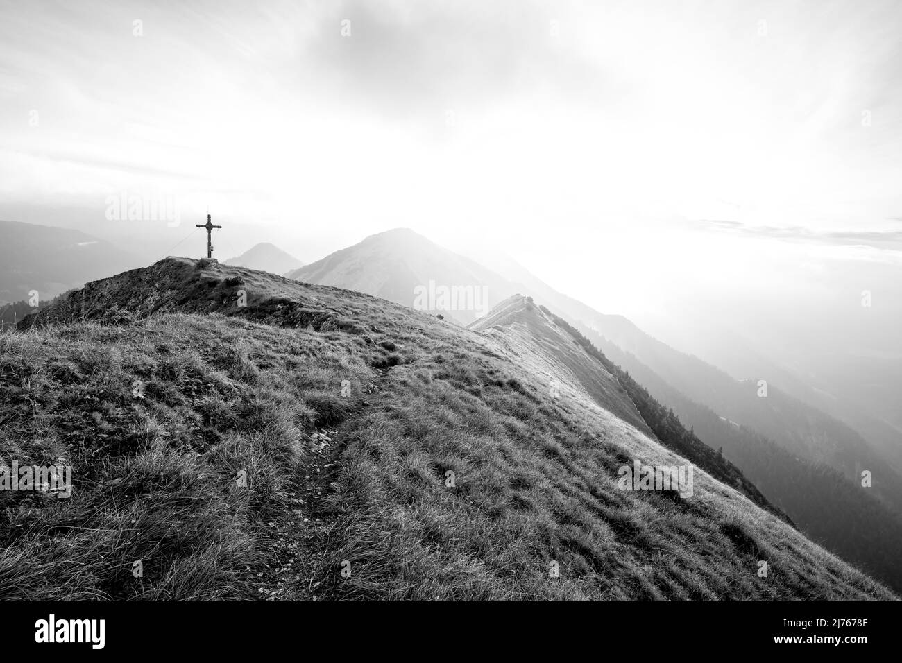 Der Gipfel der Fleischbank im Karwendel mit seinen klassischen Bergwiesen im Spätsommer bei Sonnenaufgang mit dichten Wolken und Nebel, im Hintergrund der Kompar und andere Gipfel der österreichischen Alpen. Stockfoto