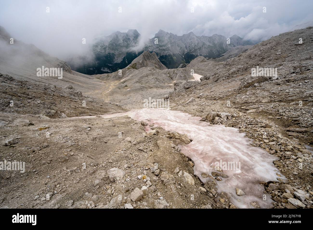 Im Hochgebirge der alpinen Hinterau-Vomper-Gebirgskette in Karwendel bleibt Staub und Sand der roten Sahara auf dem Schnee. Im Hintergrund die unwirtliche Landschaft und dichte Wolken. Stockfoto