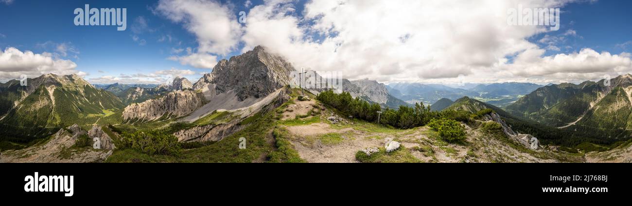 Panoramablick vom Wörnersattel bei Mittenwald im Karwendel, ncoh der bayerische Teil. In der Mitte thront der Wörner, ganz rechts und links die Soierngruppe. Die Sonne wird von einer Wolkenbank am sonst blauen Himmel versteckt. Stockfoto