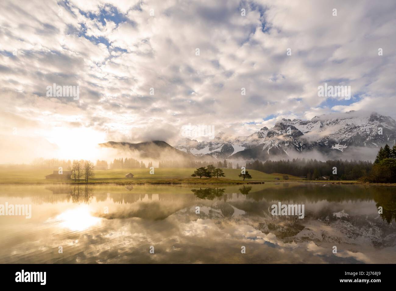 Morgenstimmung bei Sonnenaufgang am Schmalensee im bayerischen Voralpenland bei Mittenwald. Im Hintergrund das Karwendel und eine kleine Halbinsel mit einigen Bäumen. Wolken und Nebel umrahmen die Stimmung. Stockfoto