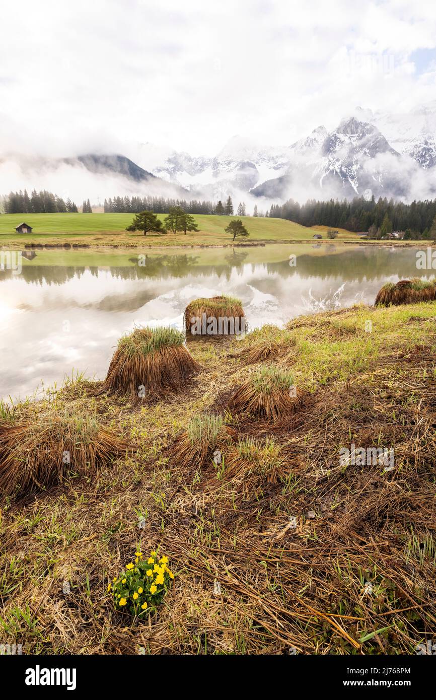 Morgenstimmung bei Sonnenaufgang am Schmalensee im bayerischen Voralpenland bei Mittenwald. Im Hintergrund das Karwendel und eine kleine Halbinsel mit einigen Bäumen. Wolken und Nebel umrahmen die Stimmung. Stockfoto