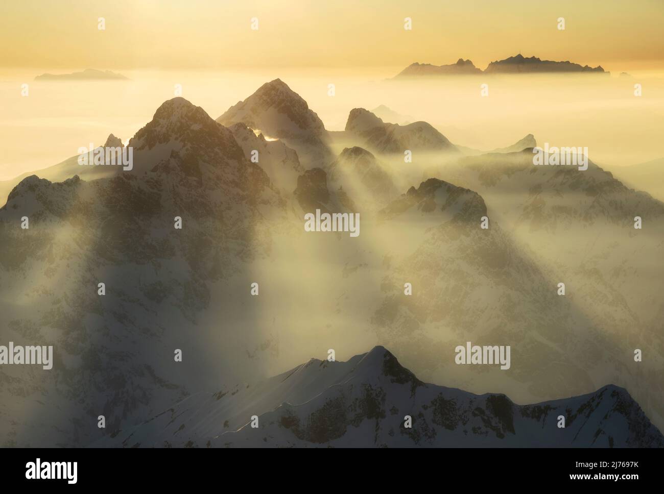 Stimmungsvoller Sonnenuntergang: Berge und Dunst werden durch warmes Sonnenlicht beleuchtet. Hochkünzelspitze und Zitterklopfen in den Lechquellen. Im Hintergrund Alpstein mit Säntis. Vorarlberg, Österreich, Schweiz, Europa Stockfoto