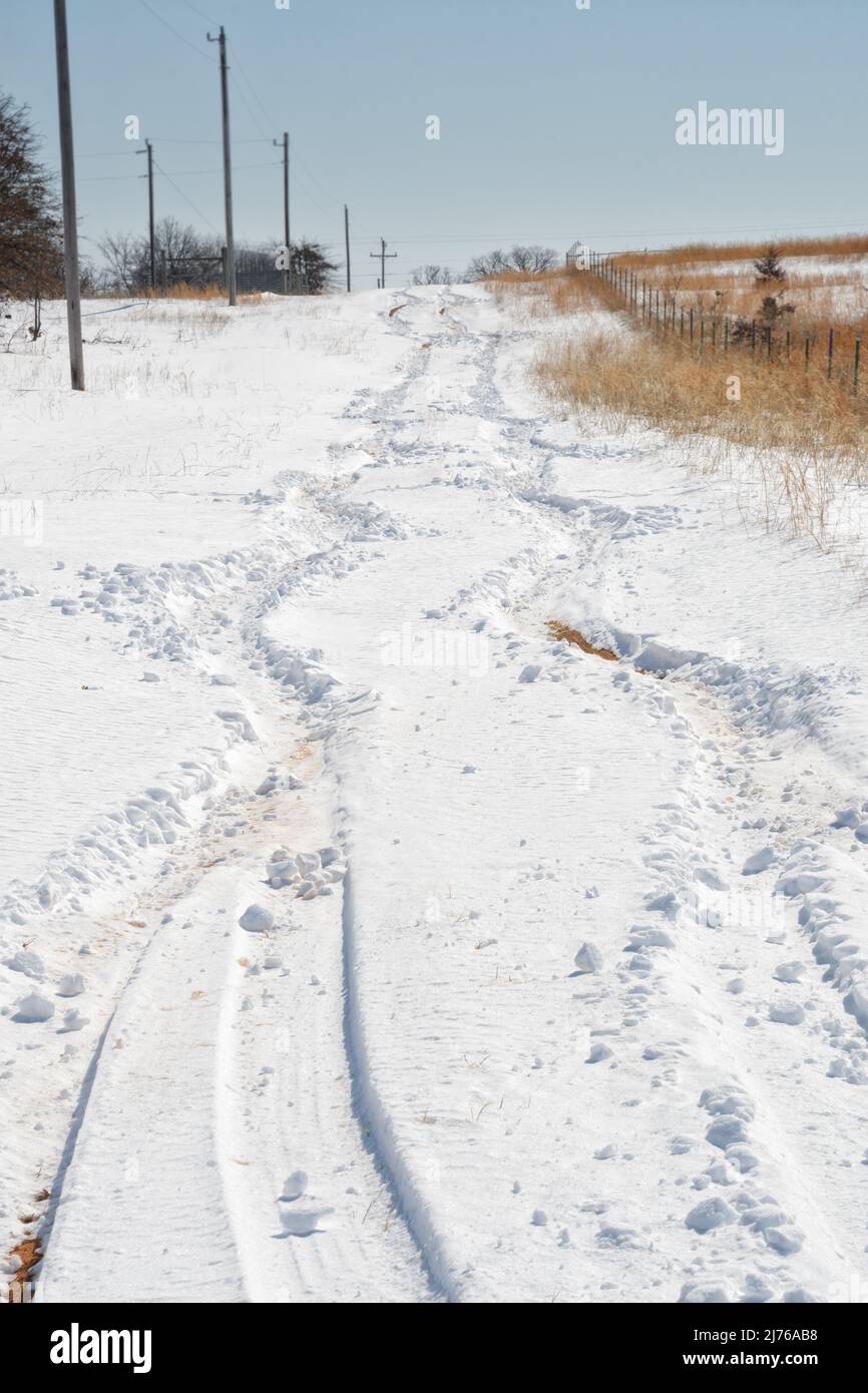 Schwankende Reifenspuren, die von einem Fahrzeug hinterlassen wurden, das nach einem Schneesturm in tiefem, unbepflügten Schnee bergauf kämpfen muss Stockfoto