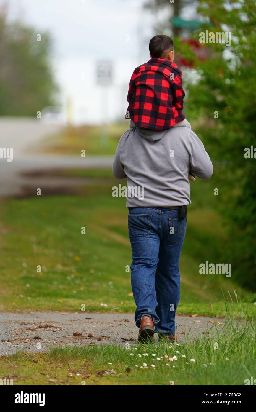 Vater mit Sohn auf den Schultern gehen die Straße hinunter. Stockfoto