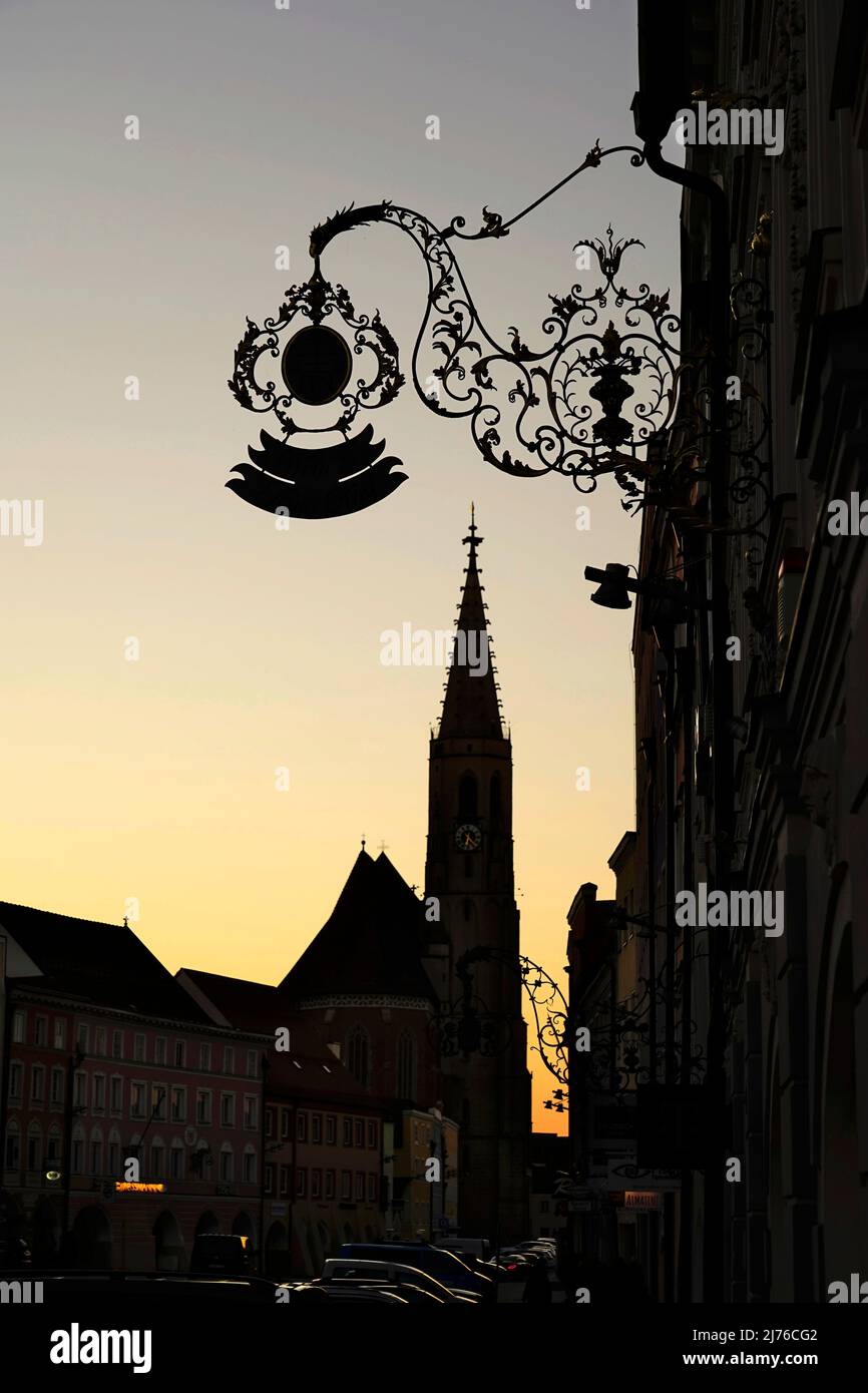 Deutschland, Bayern, Oberbayern, Altötting, Neuötting, Stadtplatz, Ludwigstraße, Pfarrkirche St. Nikolaus, Häuserzeile, schmiedeeisernes Zunftschild, Dämmerung, Silhouette Stockfoto