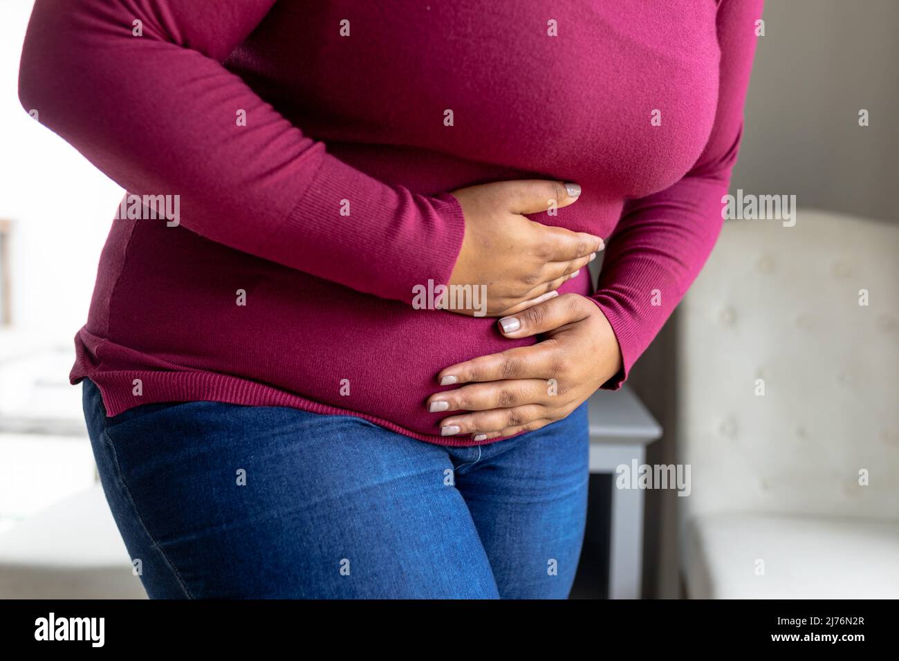 Mittelteil einer afroamerikanischen mittleren erwachsenen Frau mit Händen auf dem Bauch, die an Magenschmerzen leidet Stockfoto