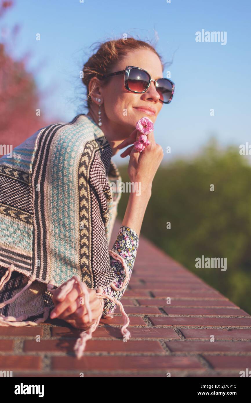Junge Rotschopf-Frau im Poncho, die im Sonnenuntergang in Sonnenbrillen träumt Stockfoto