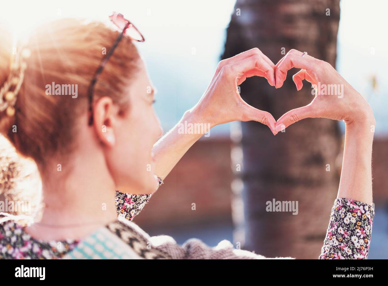 Junge Rotschopf Frau bilden Herz durch Finger in Sonnenschein, Liebeskonzept Stockfoto