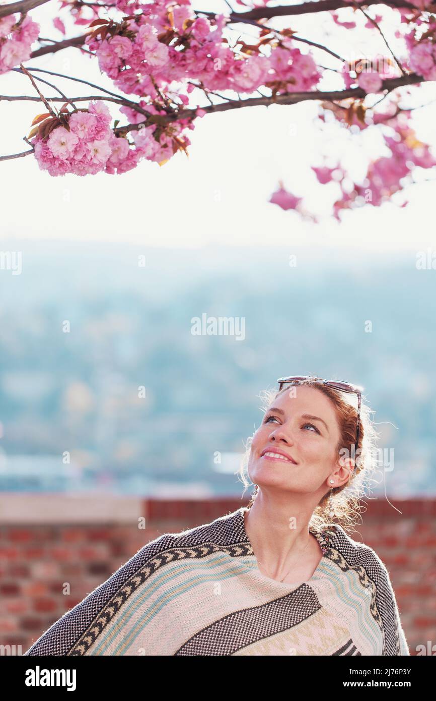 Junge rothaarige weiße Frau, die im Frühling zum Kirschbaum aufschaut, Lebensbalance Stockfoto