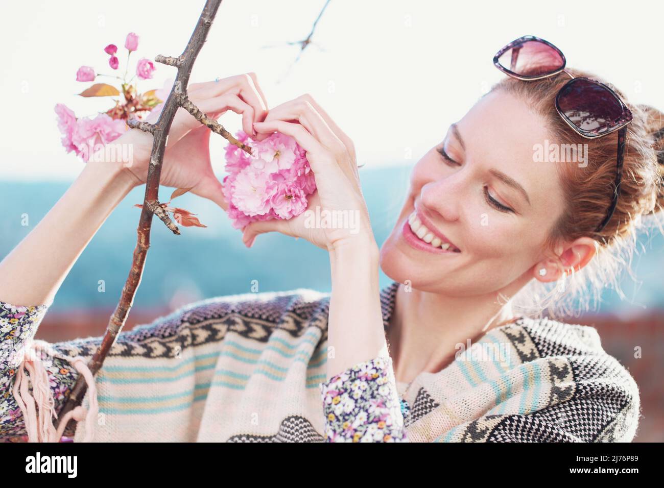 Junge Frau bildet Herz mit Kirschblüte im Freien Stockfoto