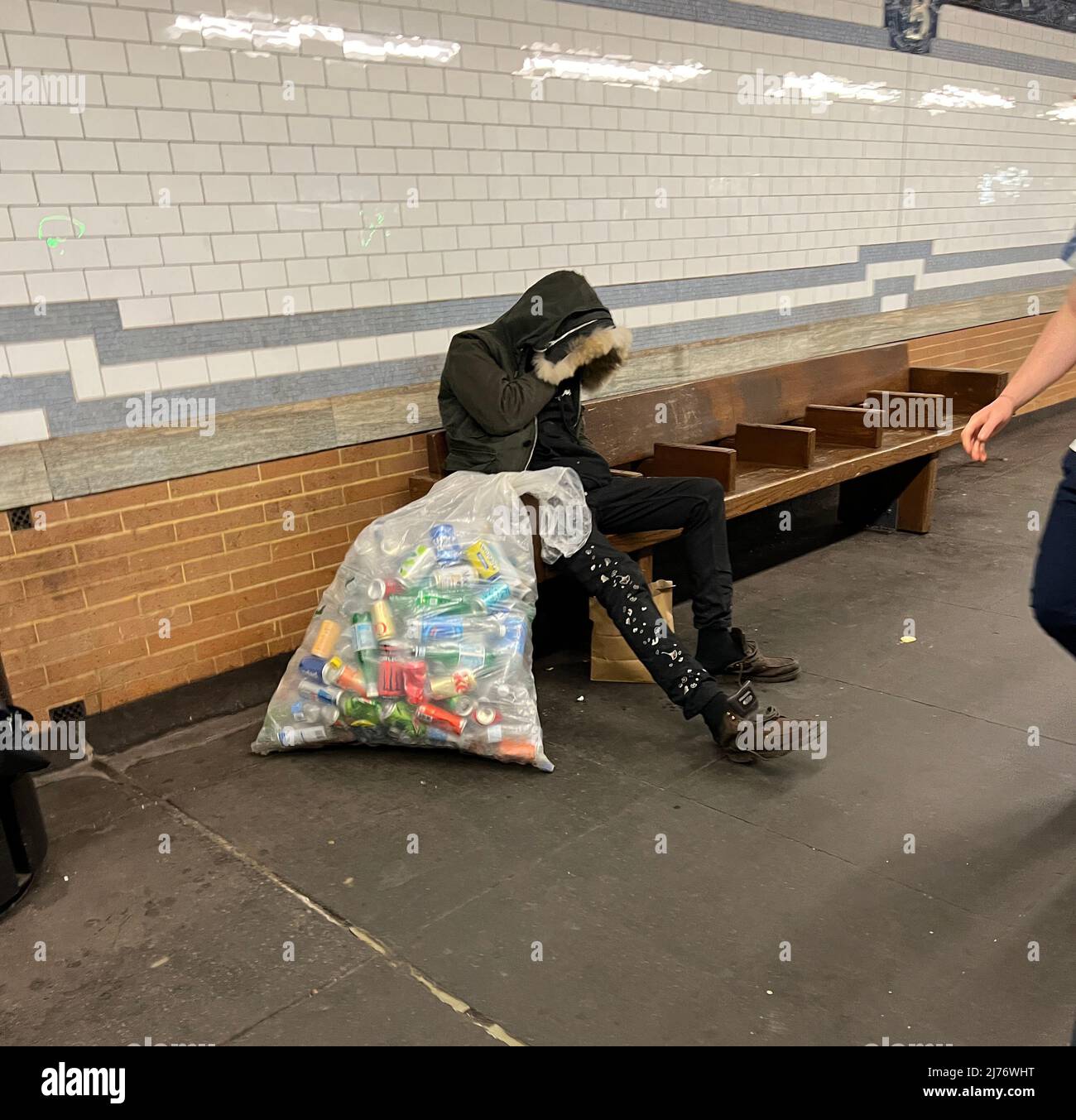 Der Mann schläft auf einer Bank auf einer U-Bahn-Plattform in Manhattan mit einer vollen Tüte Aluminiumdosen, die er gesammelt hat, um ein paar Dollar aufzukratzen. Manhattan, New York City. Stockfoto