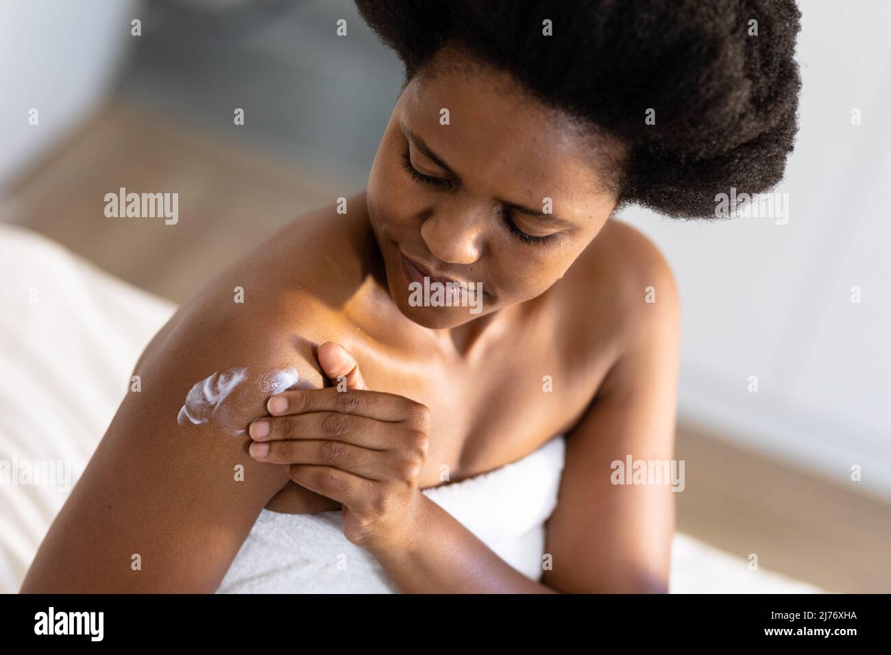 afroamerikanische Frau mit mittlerem Erwachsenen, die zu Hause Feuchtigkeitscreme auf den Arm anwendet Stockfoto