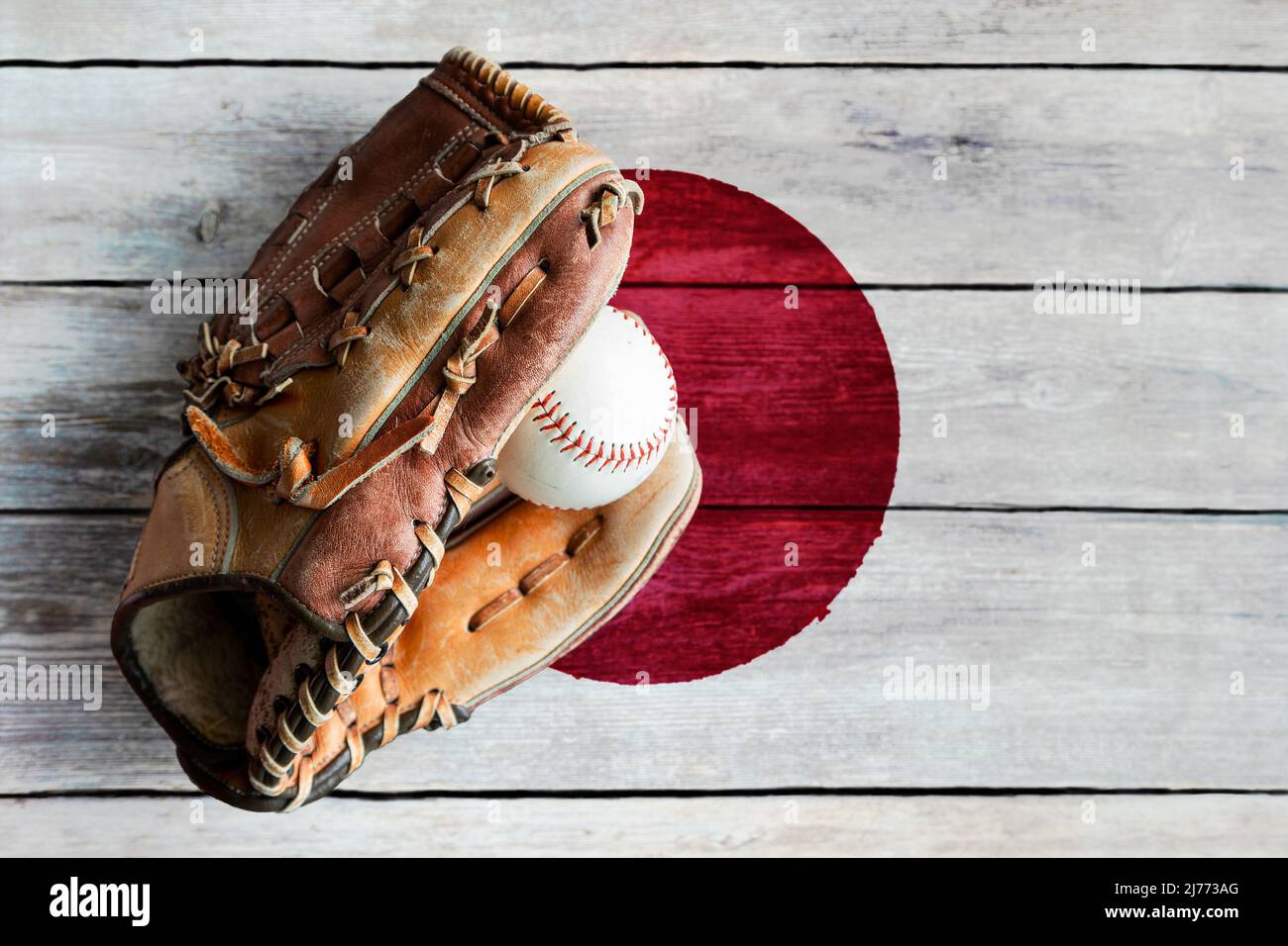Baseballhandschuh aus Leder mit Ball auf rustikalem Holzhintergrund mit bemalter japanischer Flagge und Kopierraum. Japan ist eine der besten Baseballteams der Welt Stockfoto