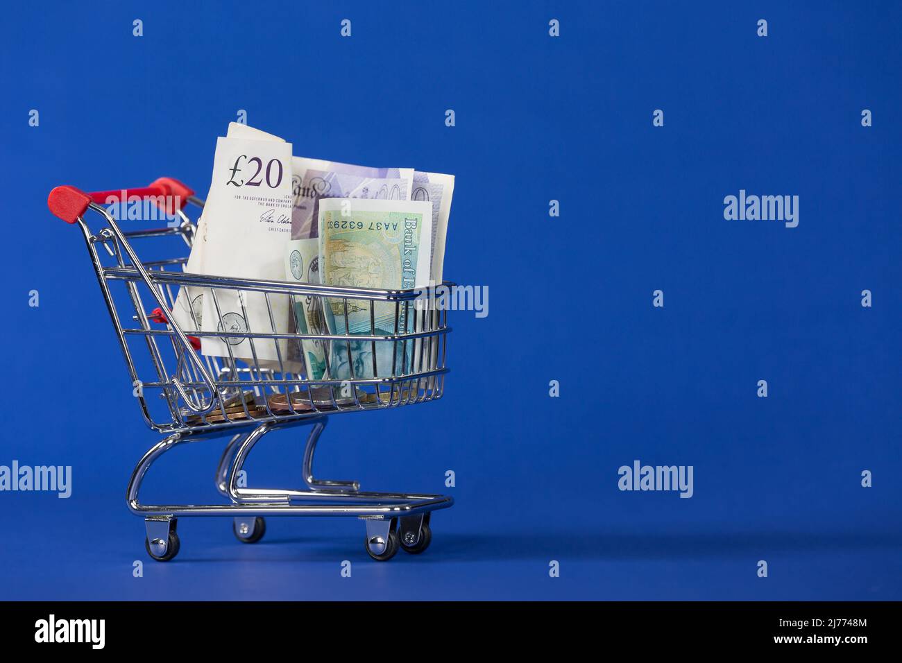 Mini-Einkaufswagen Trolly mit Geldscheine im Korb auf blauem Hintergrund Stockfoto