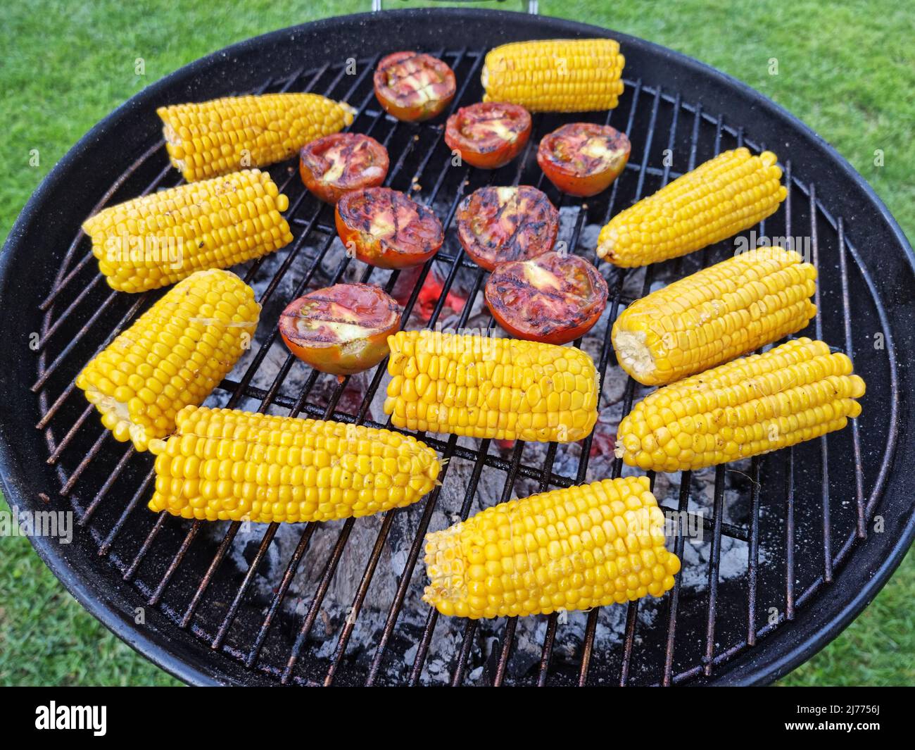 Ähre von Mais oder Mais und Tomaten auf dem Grill. Foto von Gemüse auf dem Grillrost. Kochvorgang. Stockfoto