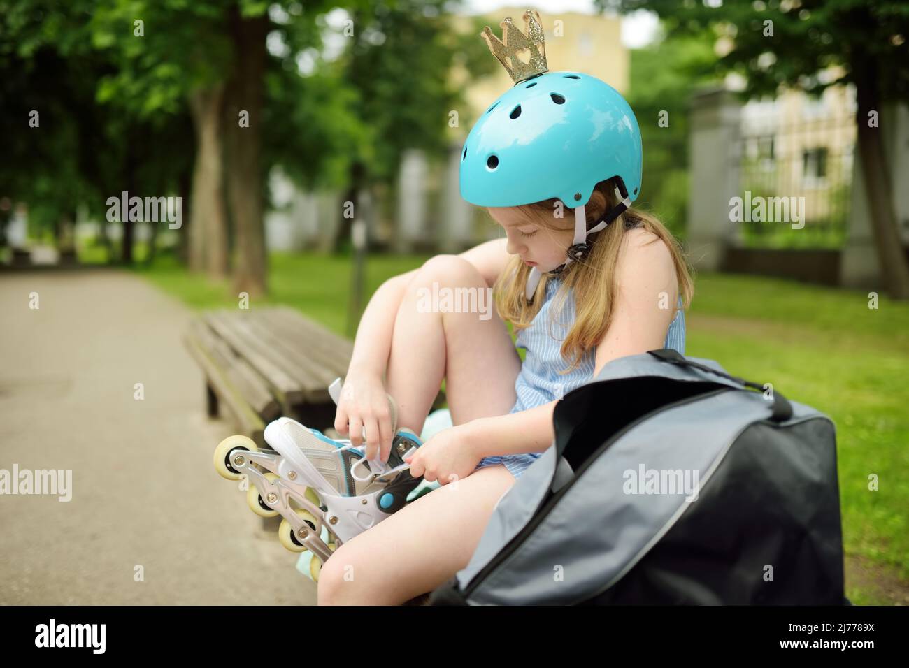 Junges Mädchen setzen auf ihre Inline-Rollschuhe an schönen Sommertag in einem Park. Kind genießt Rollschuhfahren im Freien. Stockfoto