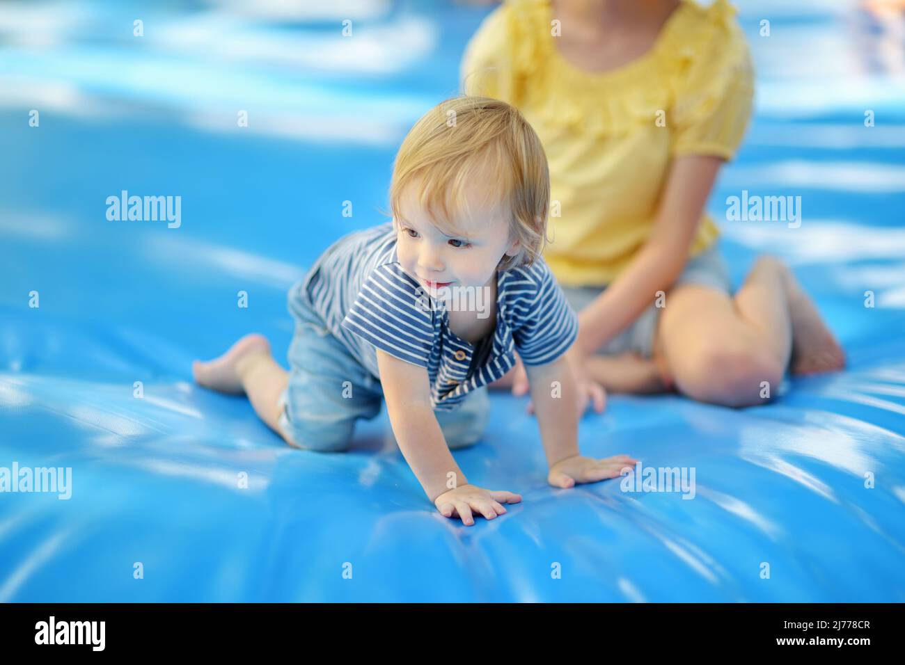Niedlicher kleiner Kleinkind Junge hüpft auf riesigen Wasser gefüllt springen Kissen. Boy springt auf und ab auf Hüpfkissen. Aktive Familienfreizeitgestaltung für Kinder und Eltern Stockfoto