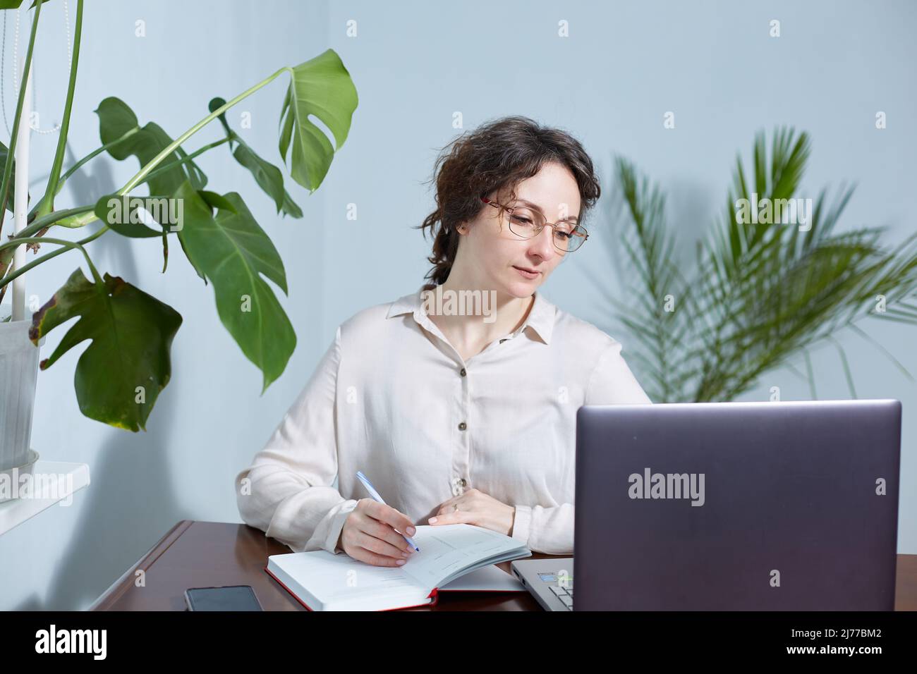 Eine Geschäftsfrau mit Brille schreibt in einem Notizbuch an ihrem Arbeitsplatz Stockfoto