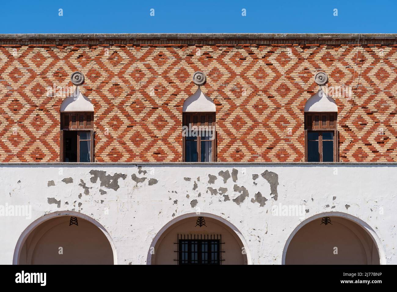 Antike Holzbogenfenster mit länglichen Balkons an einer weißen, alten Wand. Stockfoto