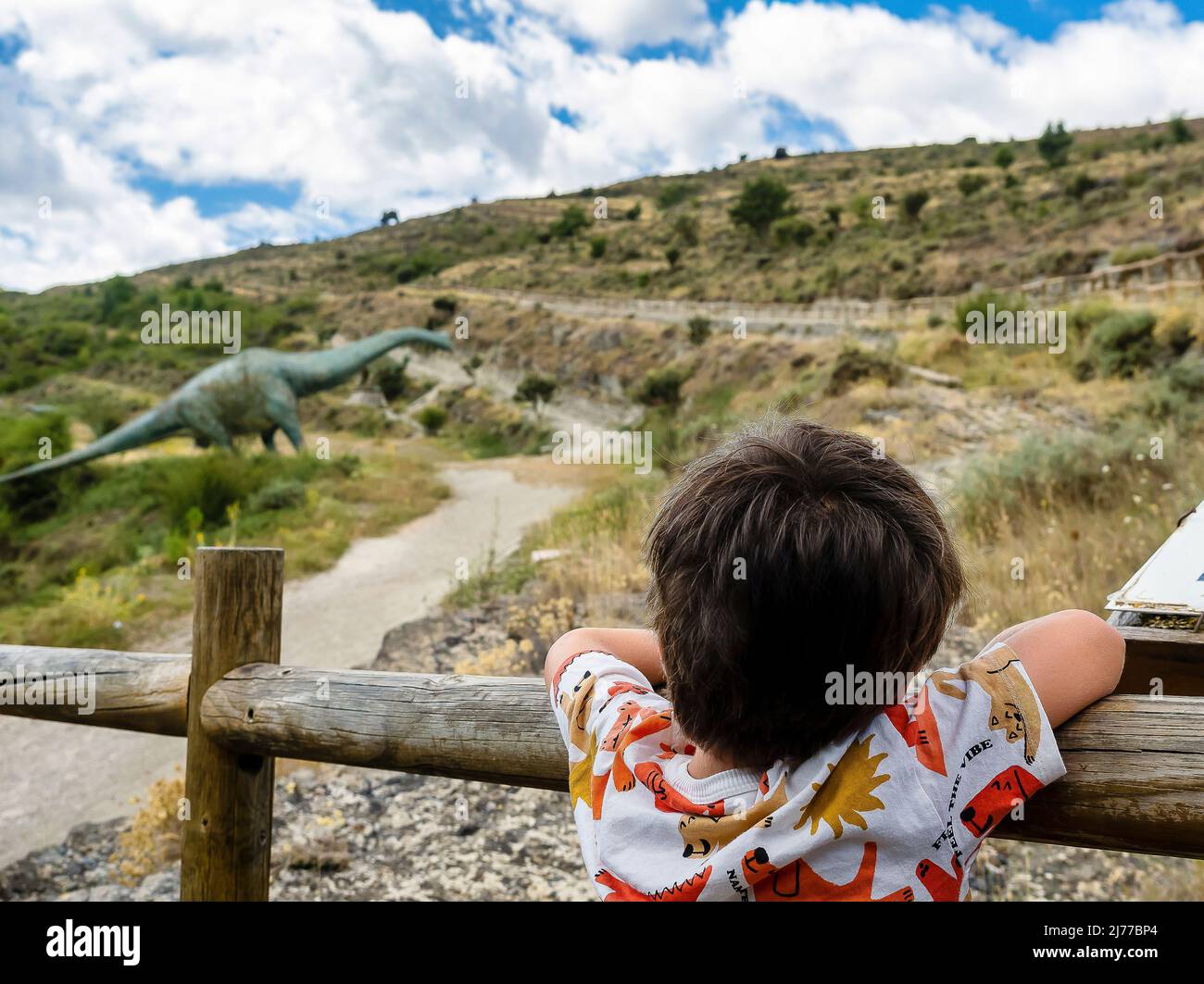 Junge, der Dinosaurier ansieht, der sich an einem Zaun lehnt Stockfoto