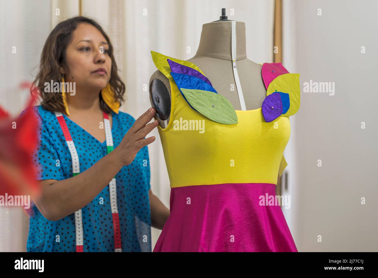 Lateinische Modedesignerin überarbeitet ein buntes Kleid auf einer Schaufensterpuppe Stockfoto
