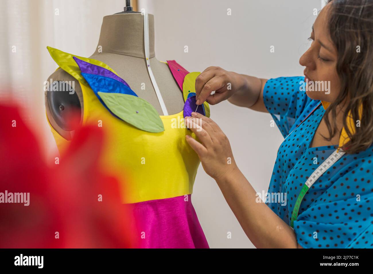 Lateinischer Modedesigner, der ein Kleid mit Nadeln an einer Schaufensterpuppe schmückt Stockfoto