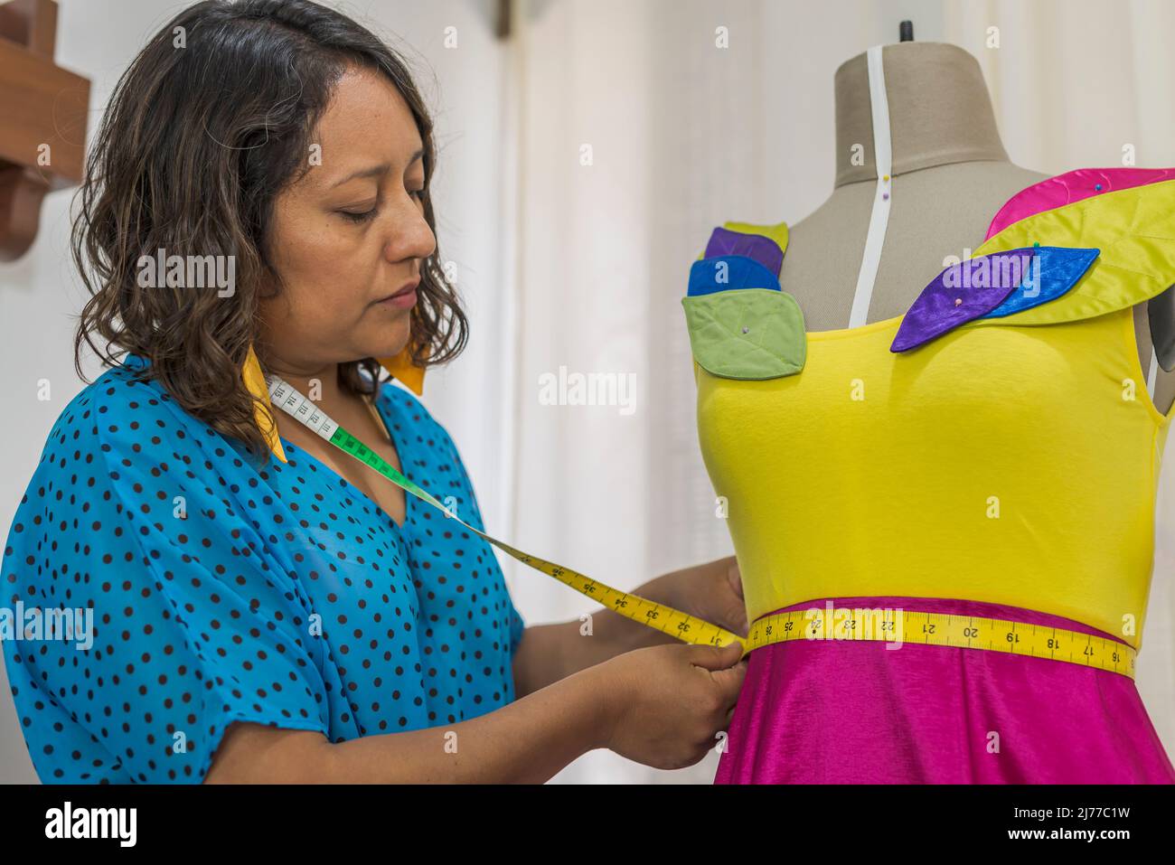 Lateinischer Modedesigner, der ein Kleid mit einem Klebeband auf einer Schaufensterpuppe misst Stockfoto